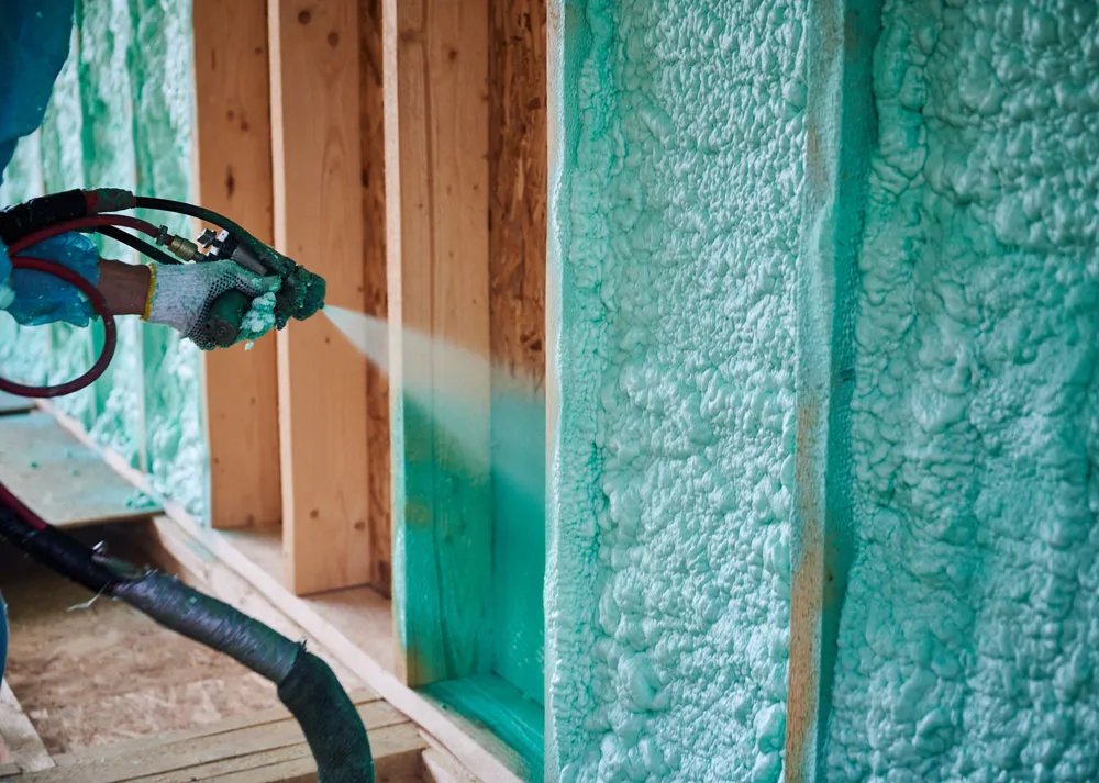 Worker applying spray foam insulation to wooden walls in a shed, showcasing energy-efficient insulation solutions for improved comfort and safety in Western Australia.