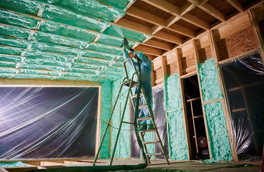 Worker applying spray foam insulation to a ceiling, showcasing energy-efficient insulation techniques in a construction setting.