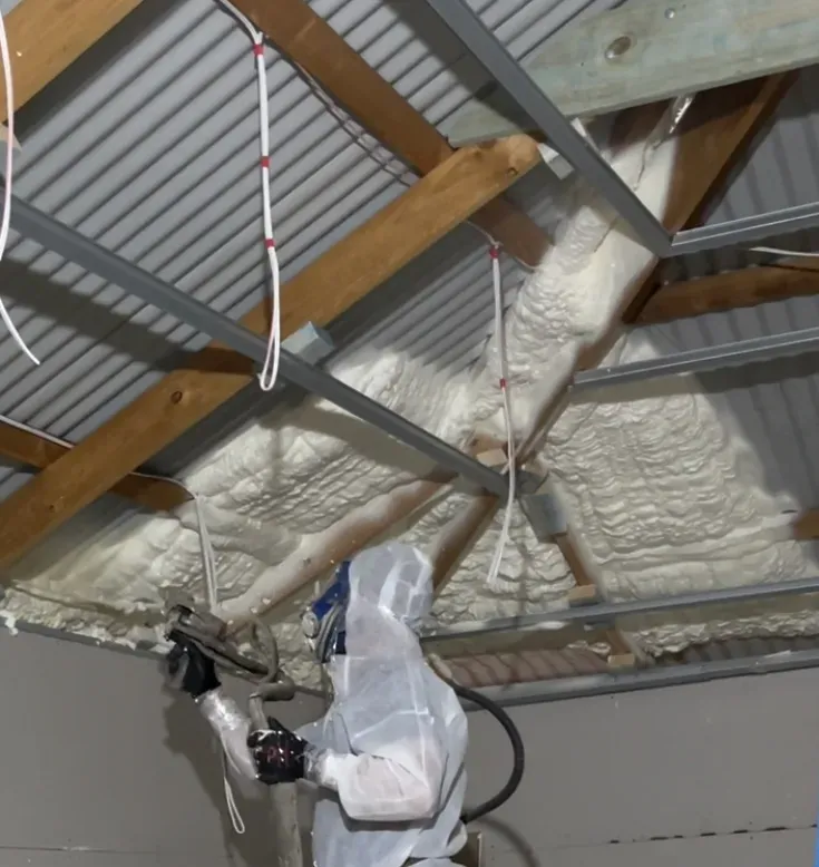 Worker applying spray foam insulation to a ceiling.
